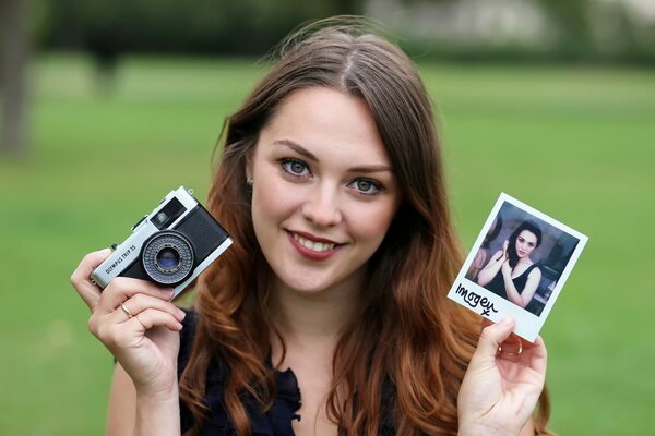 Улыбающаяся девушка с фотографией и фотоапаратом в руках
