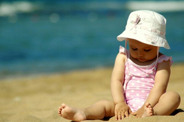 Piccola fashionista con un cappello sulla sabbia in riva al mare. Costume Da Bagno a pois