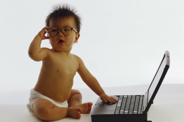 Un niño pequeño con gafas se sienta detrás de una computadora portátil