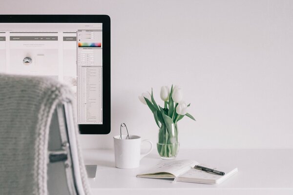 Table blanche avec livre, vase avec fleurs et ordinateur