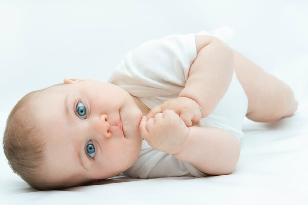 The child lies and looks with his beautiful blue eyes
