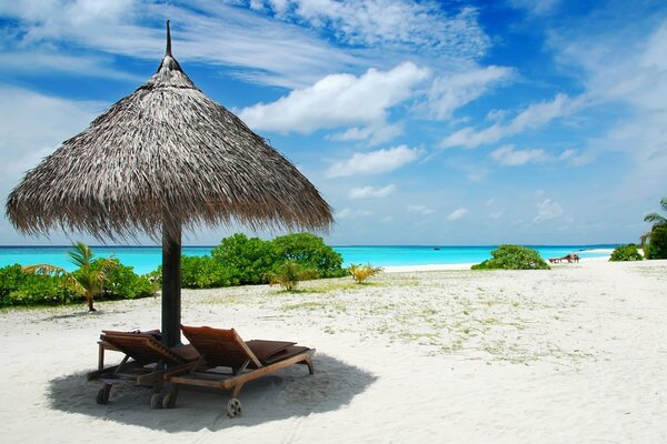 Sonnenschirm aus Stroh und Sonnenliegen am Strand