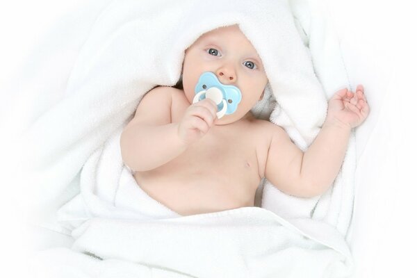 Bebé con chupete en la boca en una manta blanca