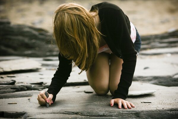 The girl draws on the asphalt with chalk