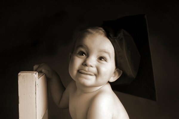 The baby shows his tongue and sits in a black beret