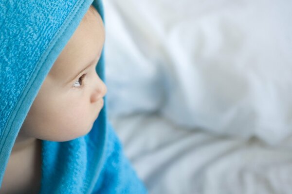 Das Kind sitzt nach dem Baden in einem blauen Handtuch