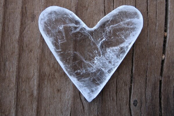 On the wooden surface there is an ice cube in the shape of a heart