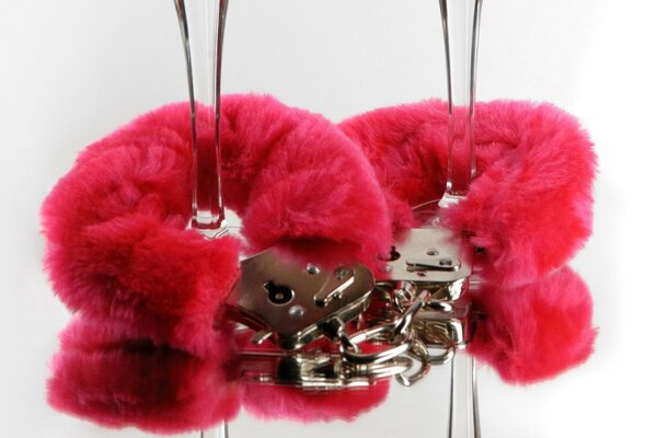 Handcuffs with red fur are attached to the legs of glasses on a white background