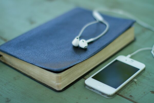 IPhone con auriculares y un libro azul al lado