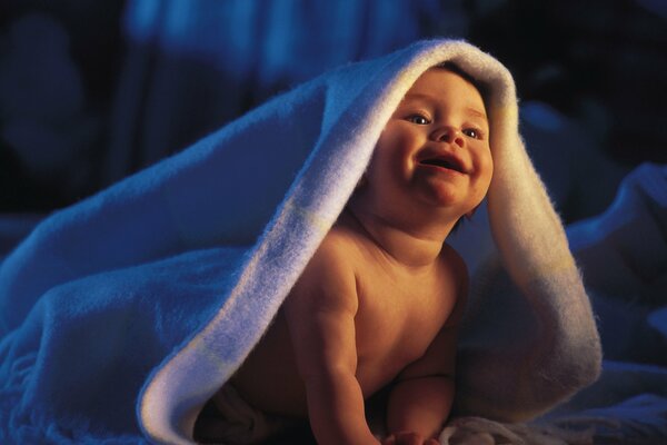 Bebé sonriendo bajo una manta blanca