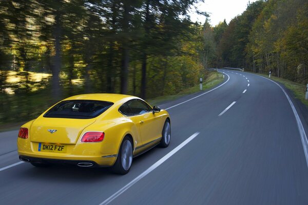 A yellow car is driving at a speed on the road