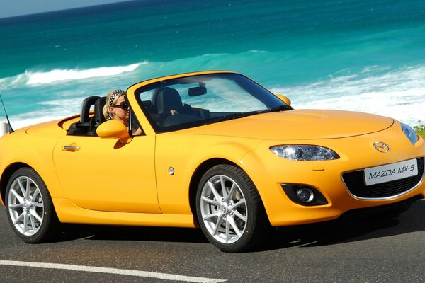 Bright yellow Mazda on the background of sea waves