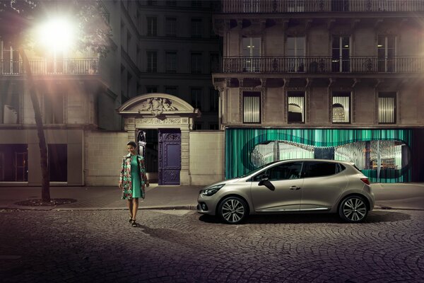 A walking girl in a coat on the background of a gray renault clio initiale paris 2014