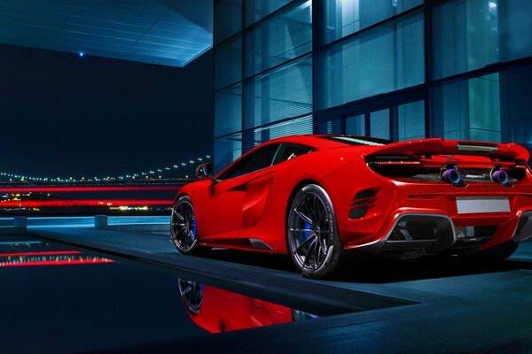 A red handsome supercar parked in front of a private house with a swimming pool on the background of a night city