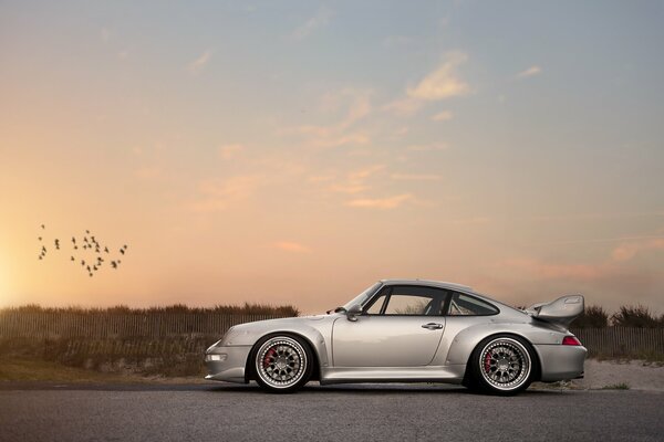 Silver Porsche on the background of the sunset sky