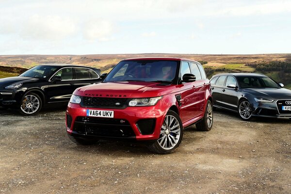 Tres coches audi, porsche, land rover, range rover en el campo