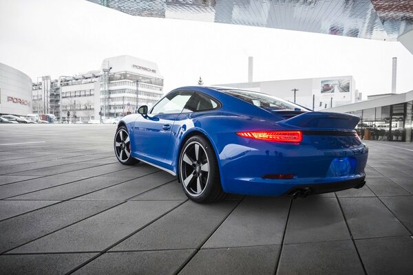 A blue Porsche 911 stands near the dealer s salon