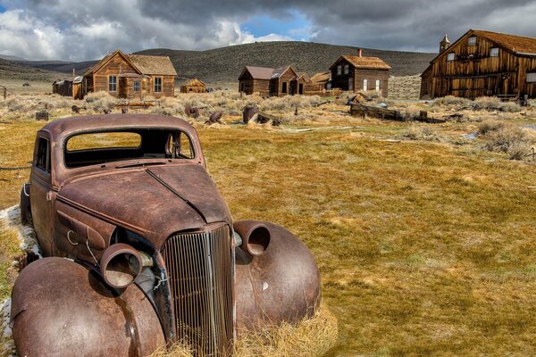 A rusty old car on the background of wooden houses