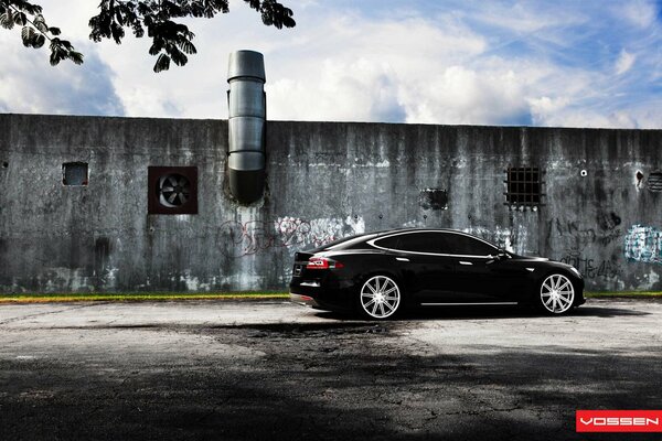 Черная Тесла модель S на фоне стены