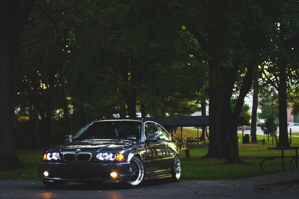 Am Abend in der Nähe des Parks von bmw, e46 mit eingeschalteten Scheinwerfern