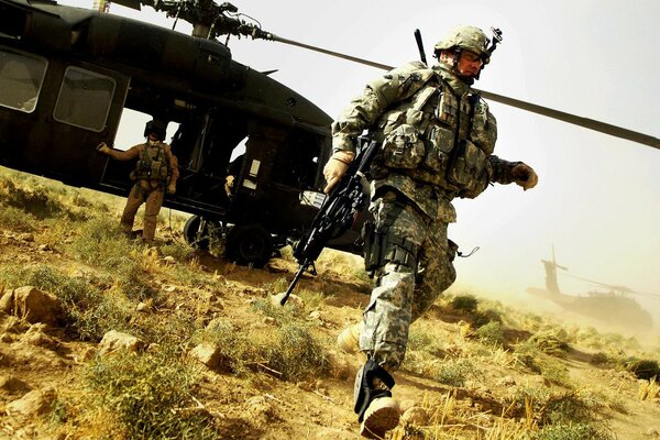 A military man with a machine gun on the background of a helicopter in the middle of the field