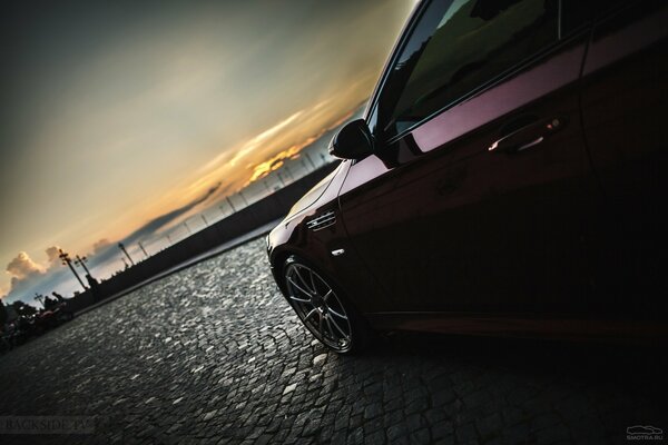 BMW rouge foncé sur le front de mer au coucher du soleil