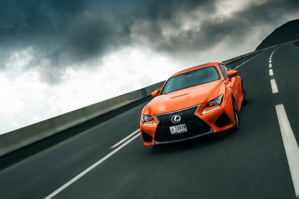 Lexus naranja corre por la pista bajo el cielo de las serpientes