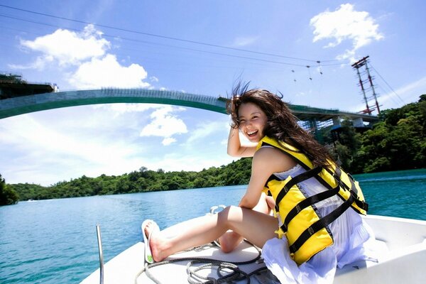 A girl in a vest on a boat. Around water, forest and clouds