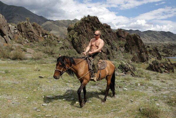 Prezydent Rosji Władimir Putin siedzący na koniu na tle gór