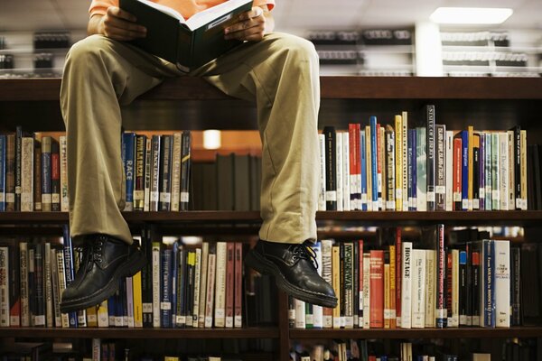 A man reads a book on a bookcase in the library