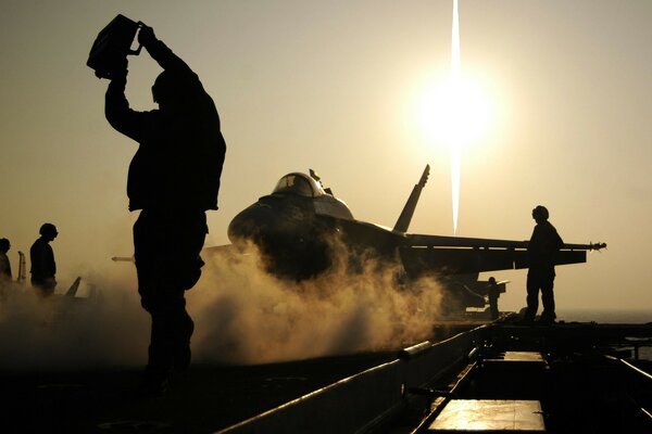 Airplane against the background of mechanics on an aircraft carrier at sunset