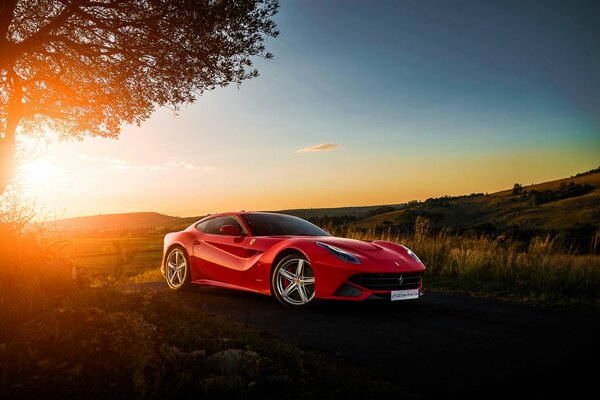 Roter Ferrari im Feld bei Sonnenuntergang Hintergrund