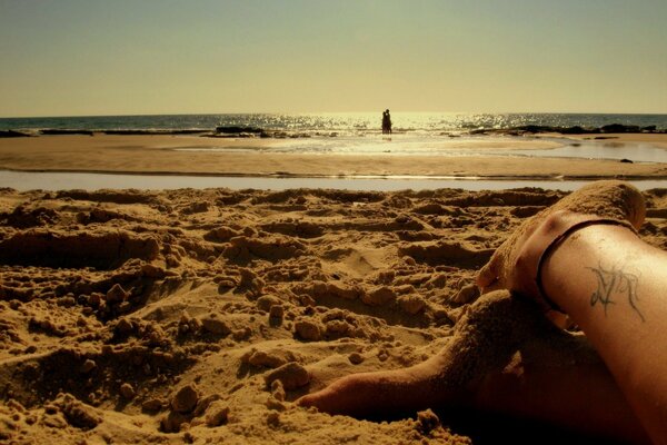 Jambes avec tatouage sur la plage sous un coucher de soleil romantique