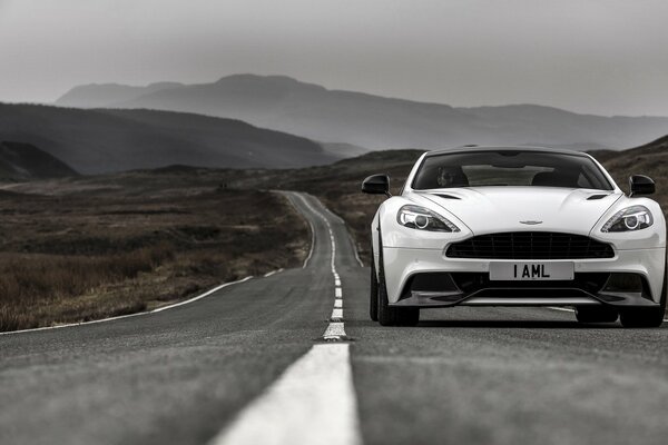 White Aston Martin rides on a boundless road among the mountains