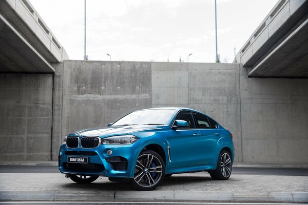 Blue BMW on the sidewalk against a gray wall