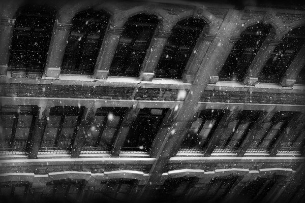 Black and white photo of an old building with windows in winter with falling snow