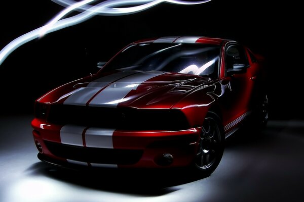 A red Ford car with two white stripes in a dark room