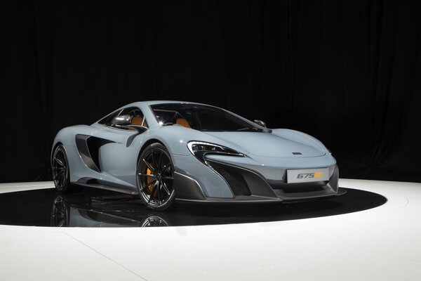 Grey McLaren car on a black circle of white floor and black background