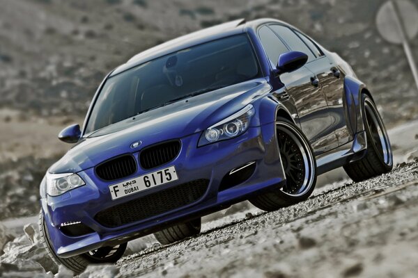 BMW M5 тюнингованная стоит на обочине дороги с щебнем