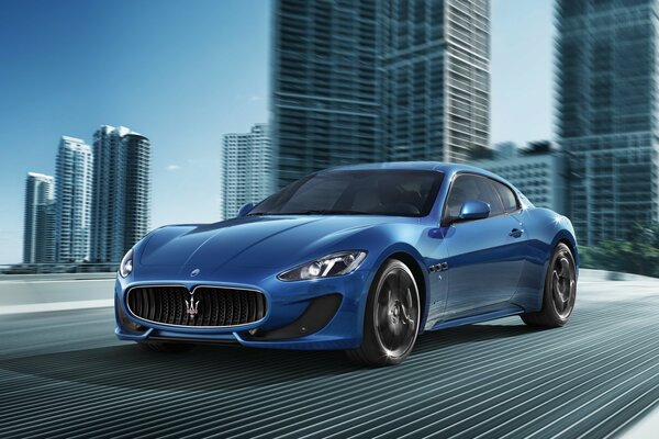 Ein blaues Auto der Firma Maserati rast über die Brücke der modernen Stadt