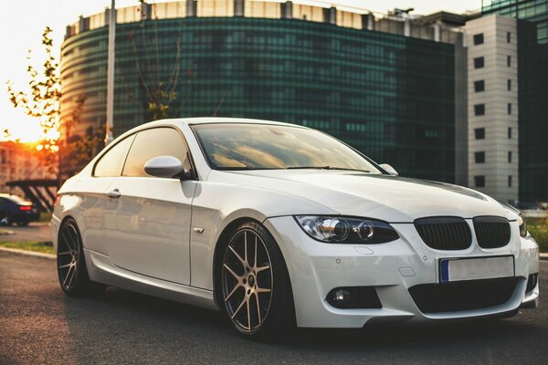 Weißes BMW-Auto auf dem Hintergrund eines Gebäudes auf der Straße bei Sonnenuntergang