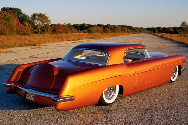 An orange retro car in the middle of an empty road