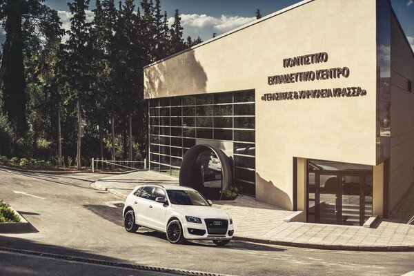 A white Audi q5 stands near a glass building