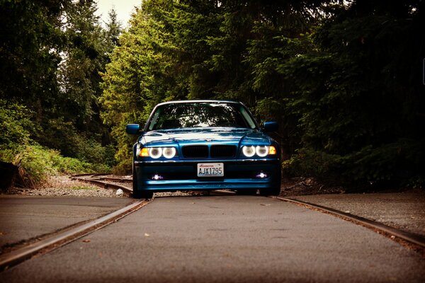 Una bmw E38 blu colorata con fari fantastici guida su una strada di campagna