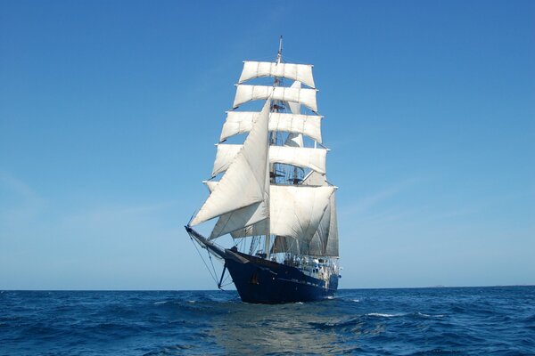 Velero de dos mástiles con velas blancas contra el mar azul y el cielo azul claro