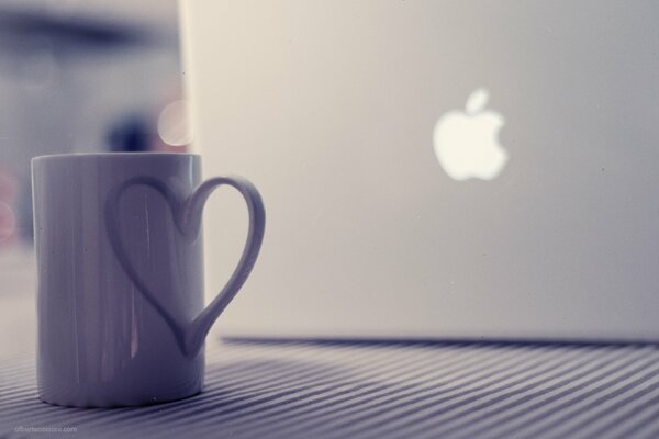 Der Becher neben dem Laptop steht auf dem Tisch