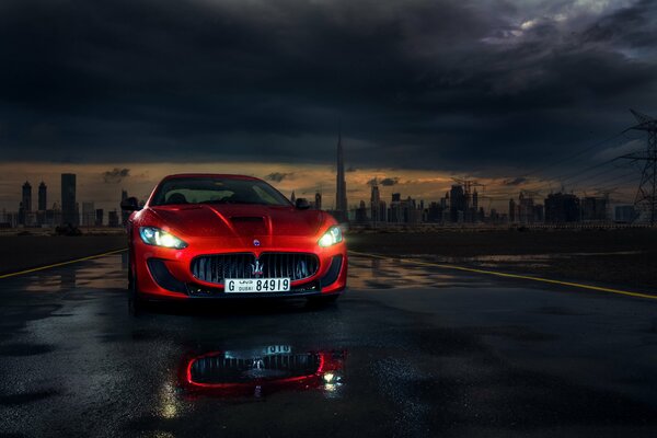 Maserati sportif rouge avec phares allumés dans la nuit sur fond de ville