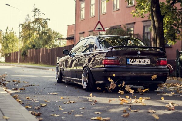 Ein schwarzer BMW fährt mit gelben Blättern entlang der Straße