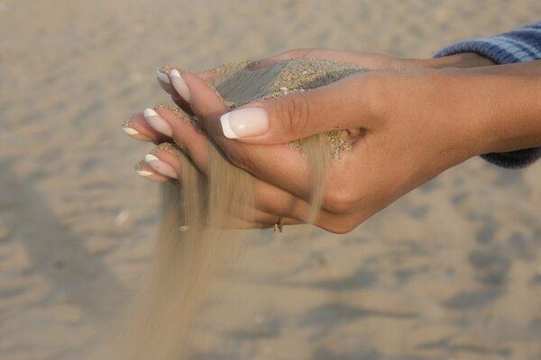 Strandsand, der durch die Finger der Frauen fließt