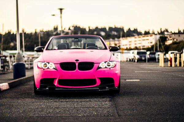 A pink BMW with angel eyes instead of a handicap is standing on the side of the road